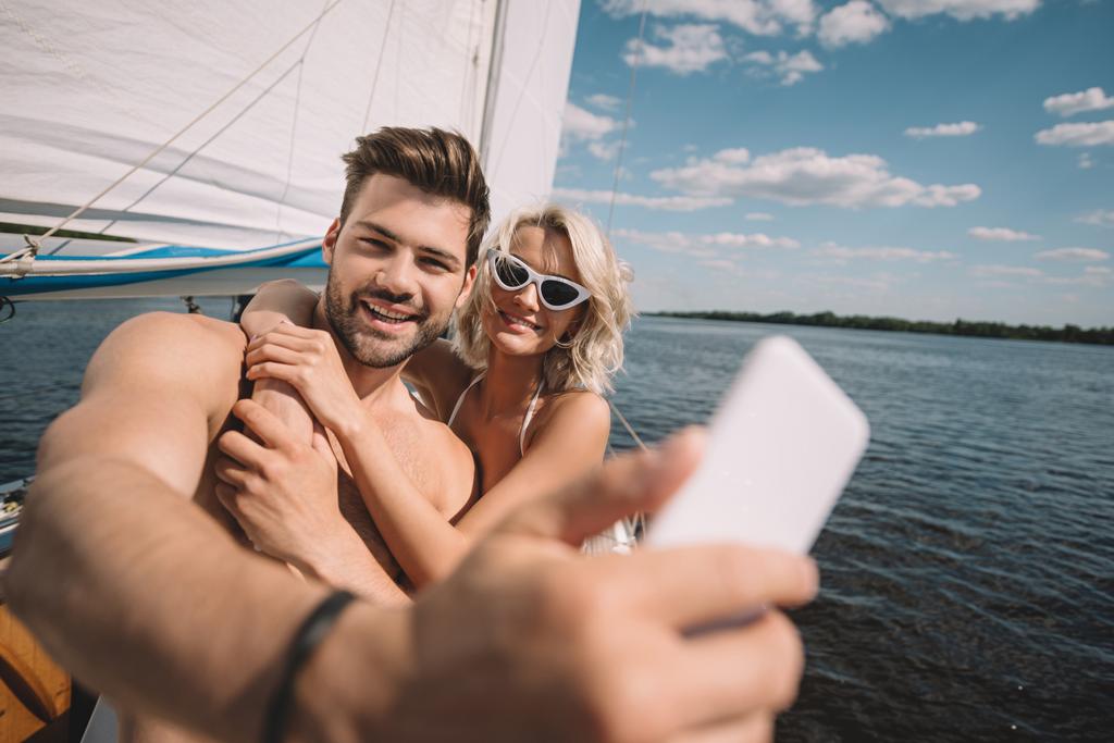 glimlachend jong koppel selfie nemen op smartphone op jacht  - Foto, afbeelding
