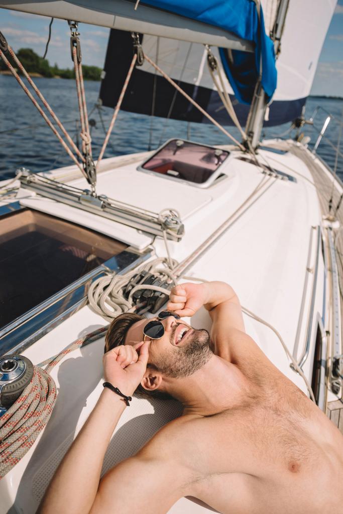 uomo muscoloso sorridente senza maglietta in occhiali da sole avendo prendere il sole su yacht
  - Foto, immagini