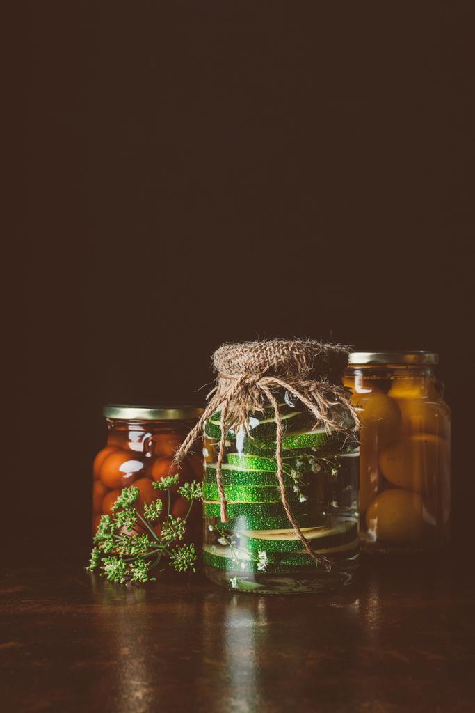 jarros de vidro com legumes preservados na mesa de madeira na cozinha escura
  - Foto, Imagem