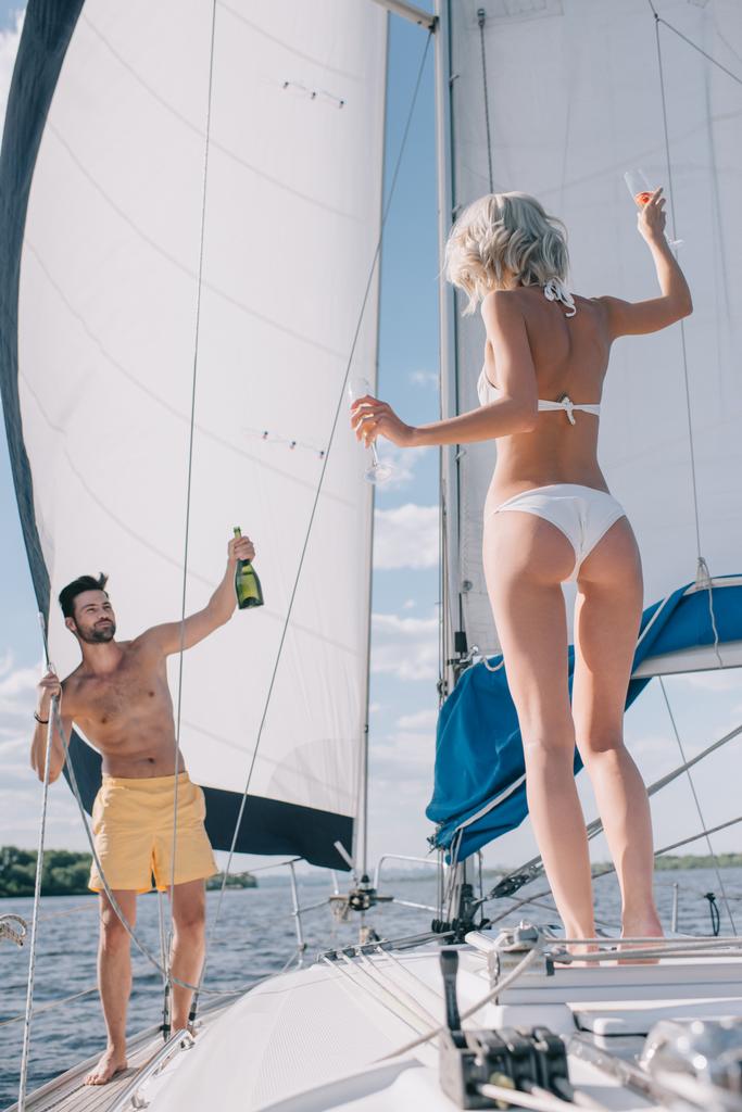knappe man van de shirtless weergegeven: fles champagne te vriendin met een bril op jacht - Foto, afbeelding