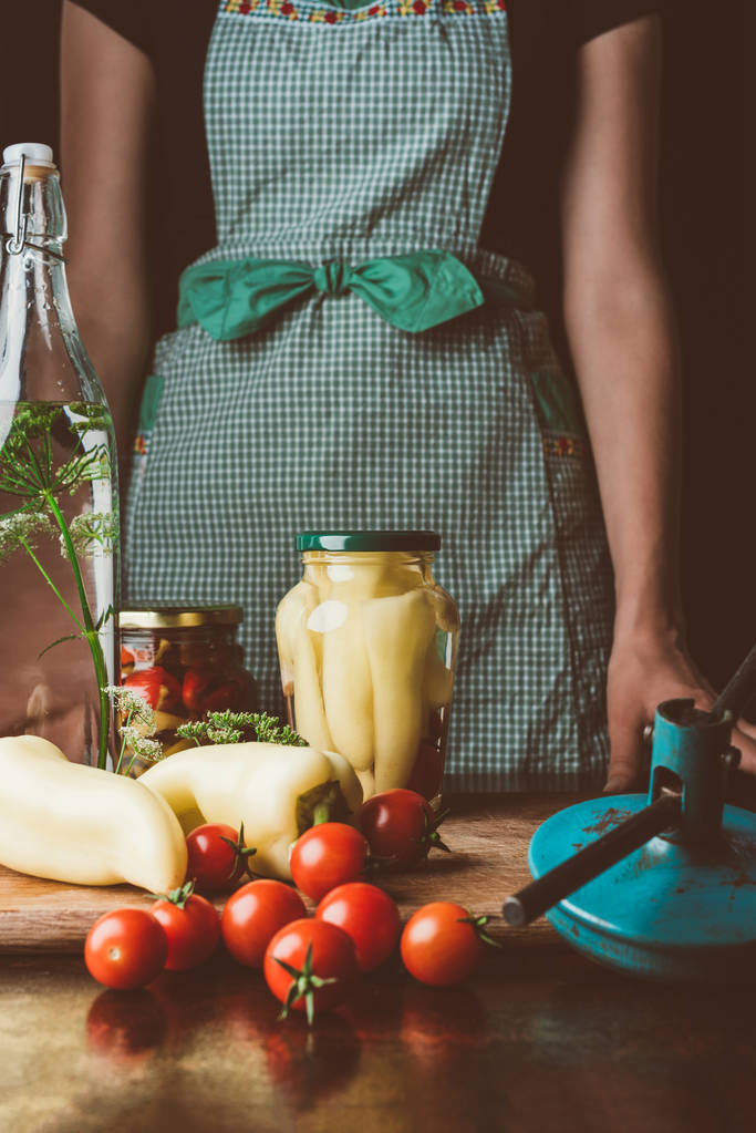 bijgesneden afbeelding van vrouw stond in de buurt van geconserveerde groenten in glazen potten op keuken - Foto, afbeelding
