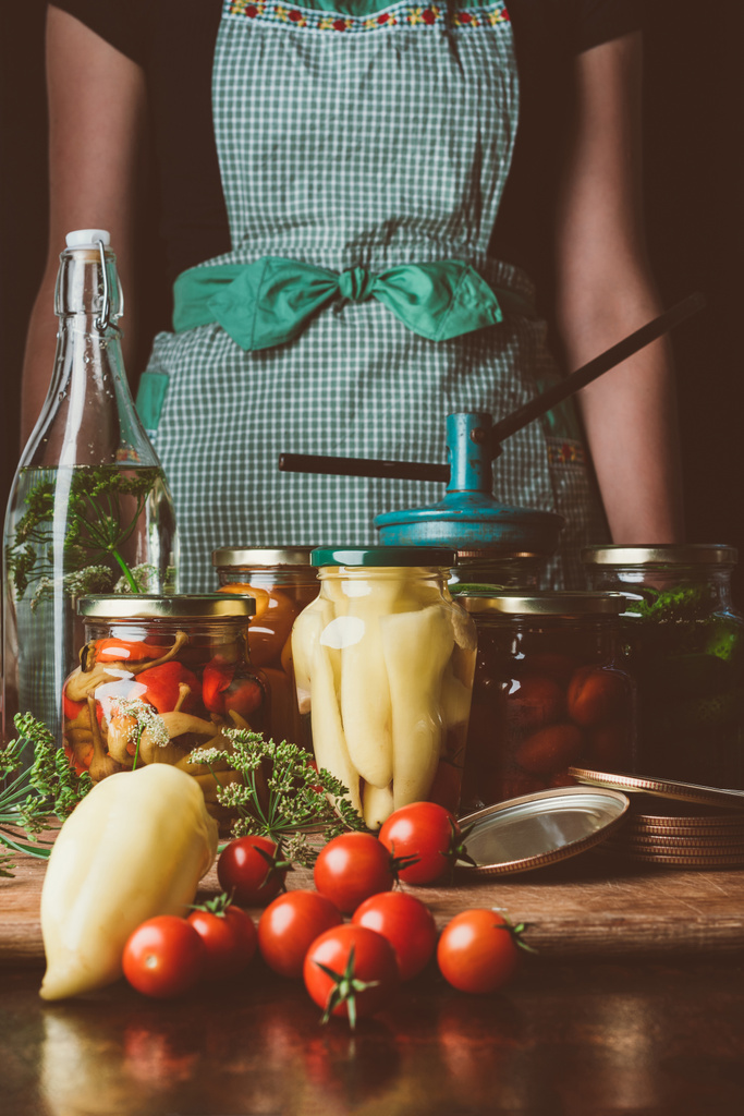 обрезанное изображение женщины, стоящей рядом с консервированными овощами в стеклянных банках на кухне
 - Фото, изображение