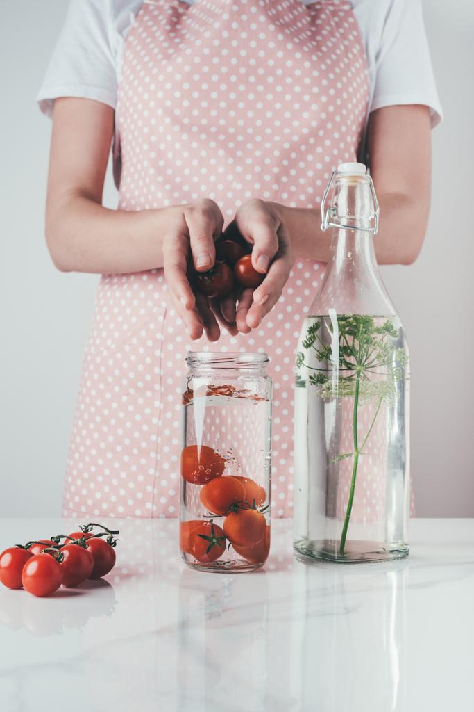 image recadrée de la femme mettant des tomates dans un bocal en verre avec de l'eau à la cuisine
 - Photo, image