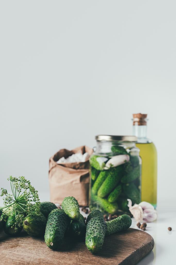 friss uborka, vágódeszka asztalra és konzerv uborka üvegedénybe háttér - Fotó, kép