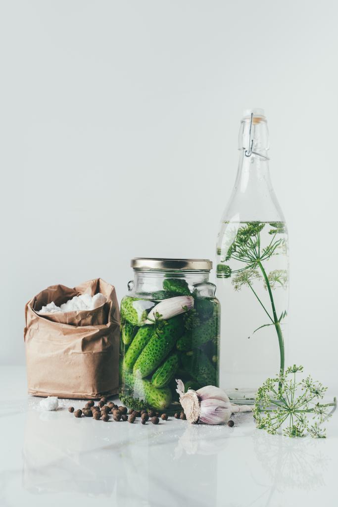 jarra de vidro com pepinos preservados, garrafa de vidro com endro e sal na mesa
 - Foto, Imagem
