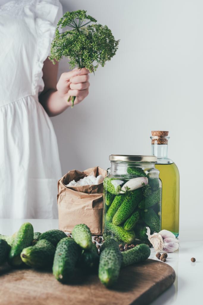 cropped image of woman preparing preserved organic cucumbers and holding dill at kitchen - Photo, Image