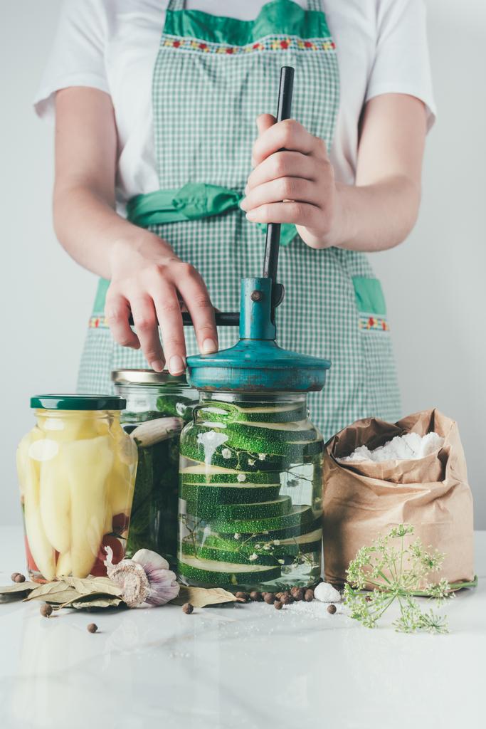 περικομμένη εικόνα γυναίκας προετοιμασία διατηρημένα κολοκυθάκια στην κουζίνα - Φωτογραφία, εικόνα