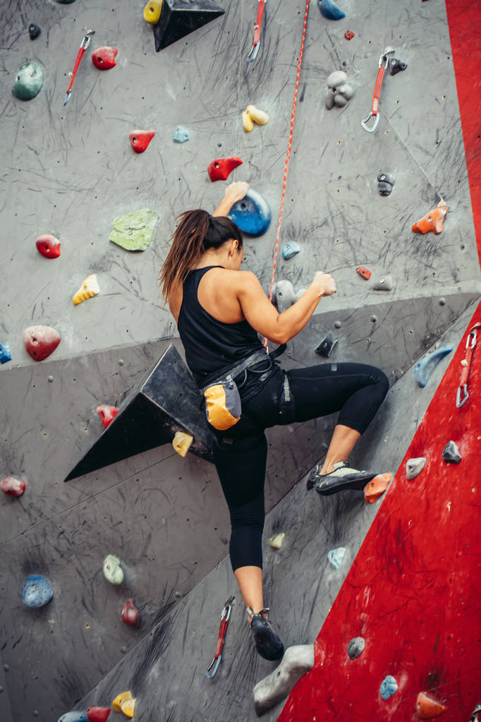 Mujer joven deportiva entrenando en un colorido gimnasio de escalada. Chica escaladora libre subiendo a interior - Foto, imagen