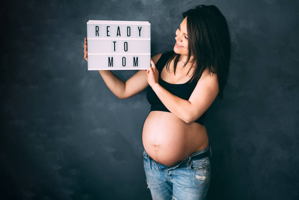 Красива вагітна жінка насолоджується життям, посміхається і позує на камеру з великим животом
 - Фото, зображення