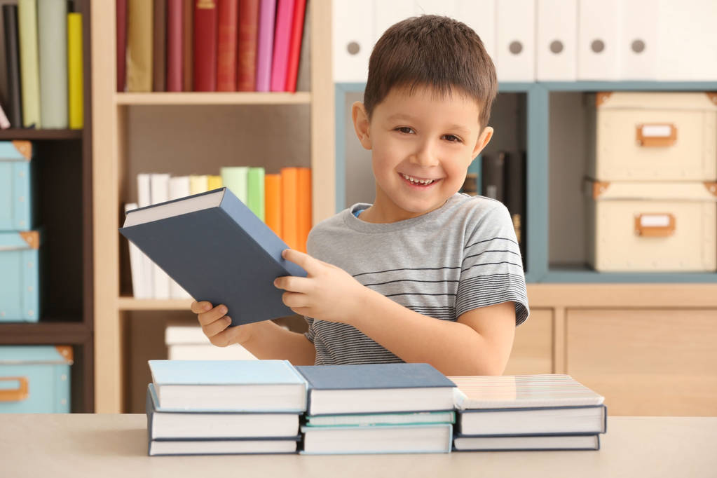 Netter kleiner Junge mit vielen Hausaufgaben in der Bibliothek - Foto, Bild