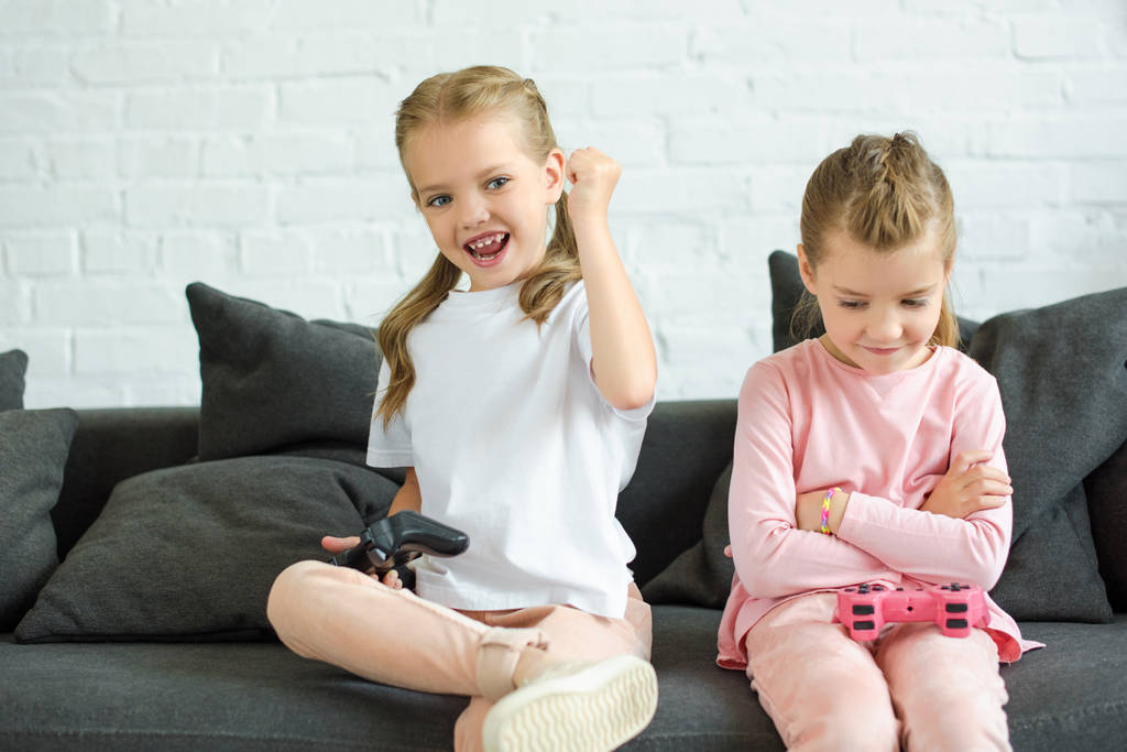 entzückende kleine Schwestern mit Gamepads beim gemeinsamen Videospiel zu Hause - Foto, Bild