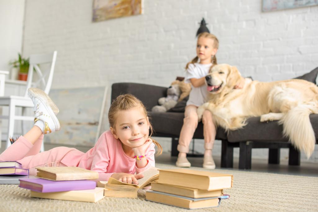 Wyostrzanie małych sióstr z książek i golden retriever pies w pobliżu przez w domu - Zdjęcie, obraz