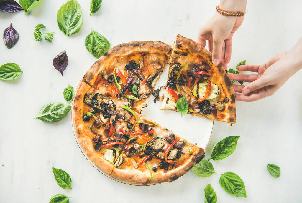 weibliche Hand mit frisch gebackener italienischer vegetarischer Pizza mit Gemüse und frischem Basilikum über weißem Marmortisch - Foto, Bild