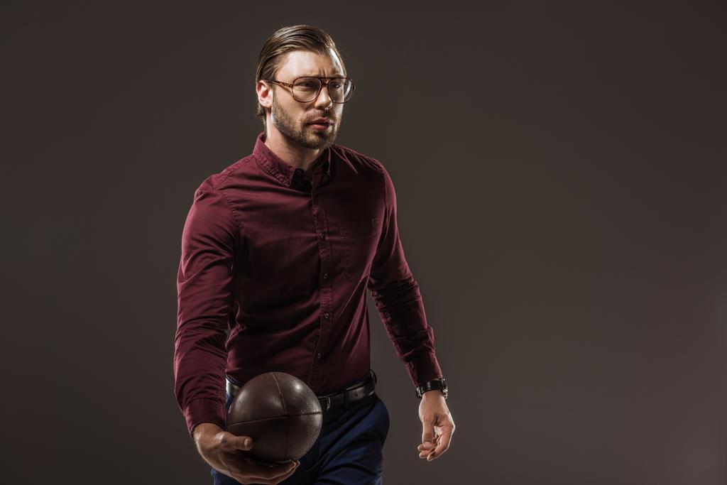 όμορφος άνδρας σε γυαλιά κρατώντας την μπάλα του ράγκμπι και αναζητούν μακριά απομονώνονται σε μαύρο - Φωτογραφία, εικόνα