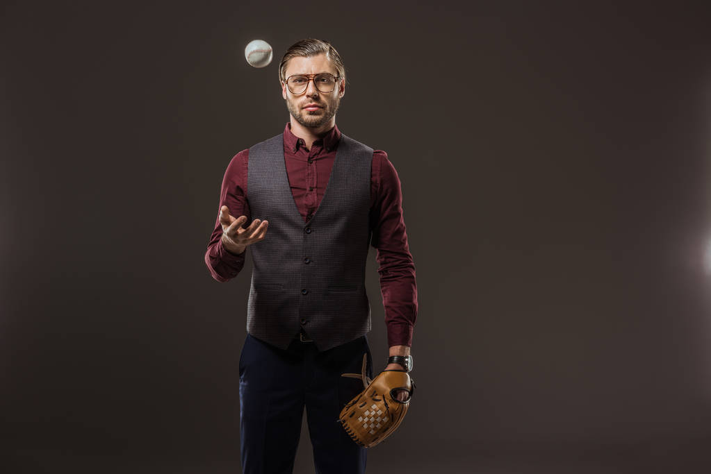 homem de negócios sério com luva de beisebol jogando bola e olhando para a câmera isolada no preto
 - Foto, Imagem
