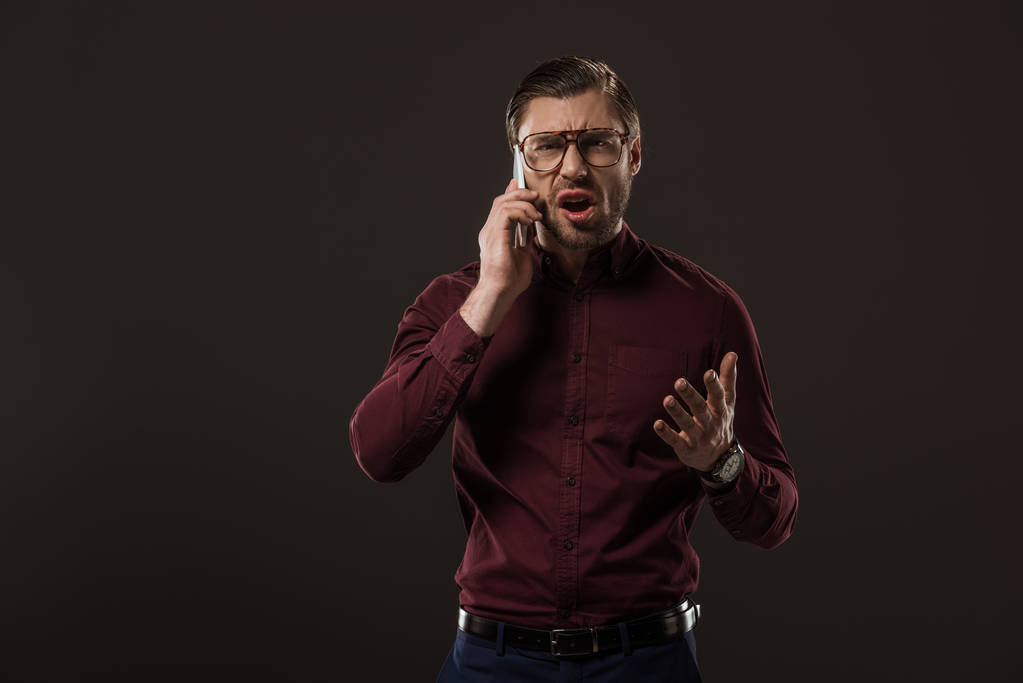 сердитий чоловік в окулярах розмовляє по смартфону ізольовано на чорному
 - Фото, зображення