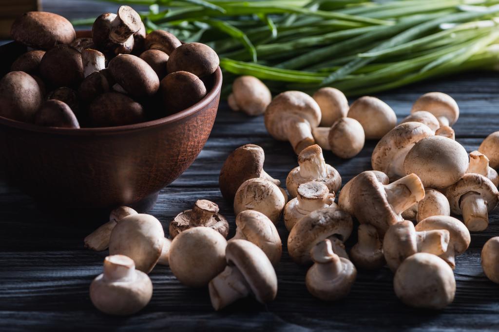 Nahaufnahme roher Champignon-Pilze mit Zwiebeln auf dunklem Holztisch - Foto, Bild