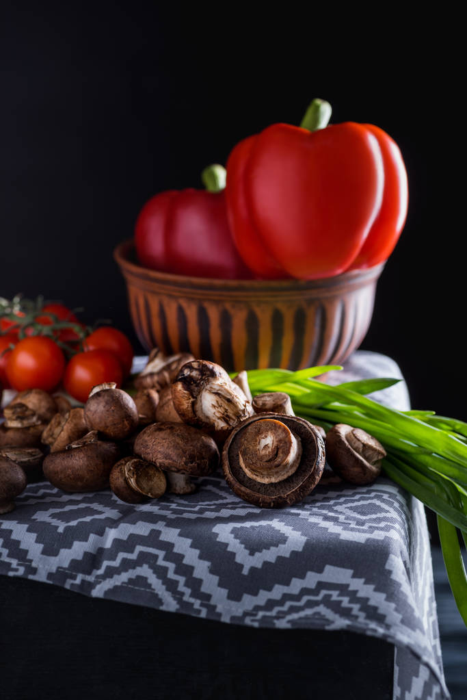 Nahaufnahme roher Champignon-Pilze mit Gemüse auf blauer Serviette auf schwarz - Foto, Bild