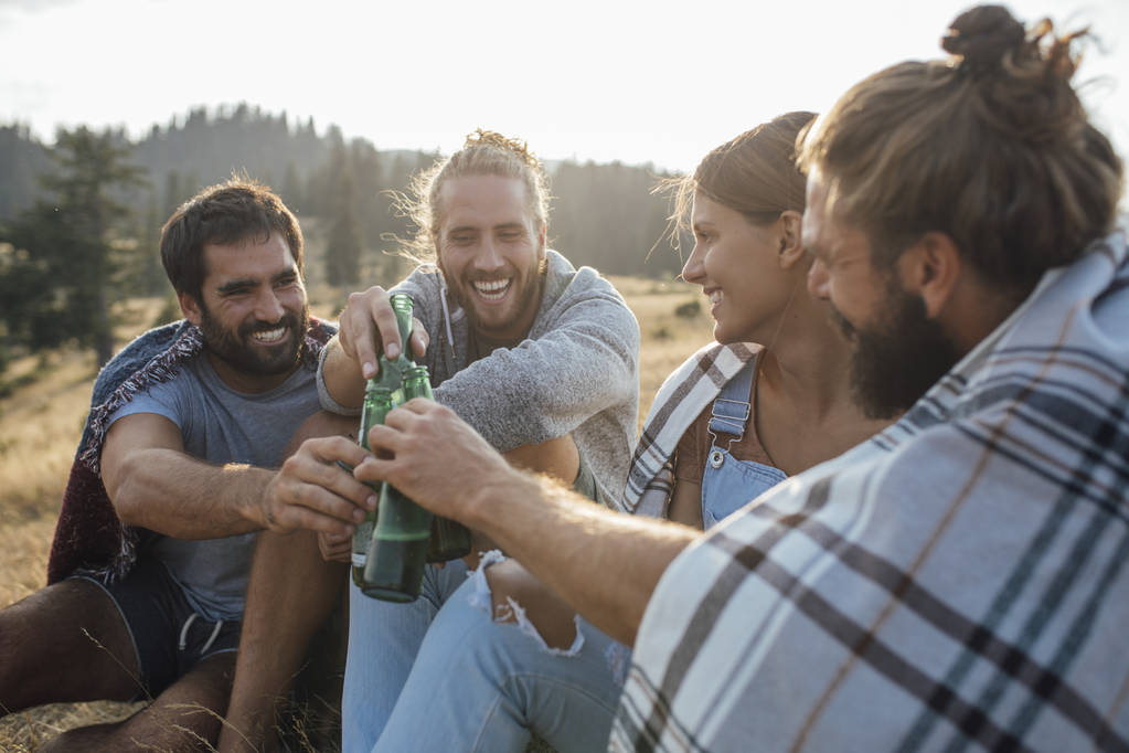Группа молодых людей пьет пиво на природе и выглядит счастливой.
. - Фото, изображение