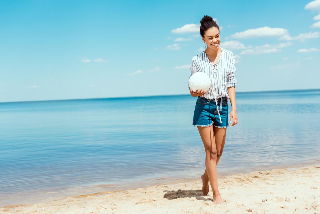 砂浜のビーチでバレーボールのボールを保持している幸せのアフリカ系アメリカ人女性  - 写真・画像