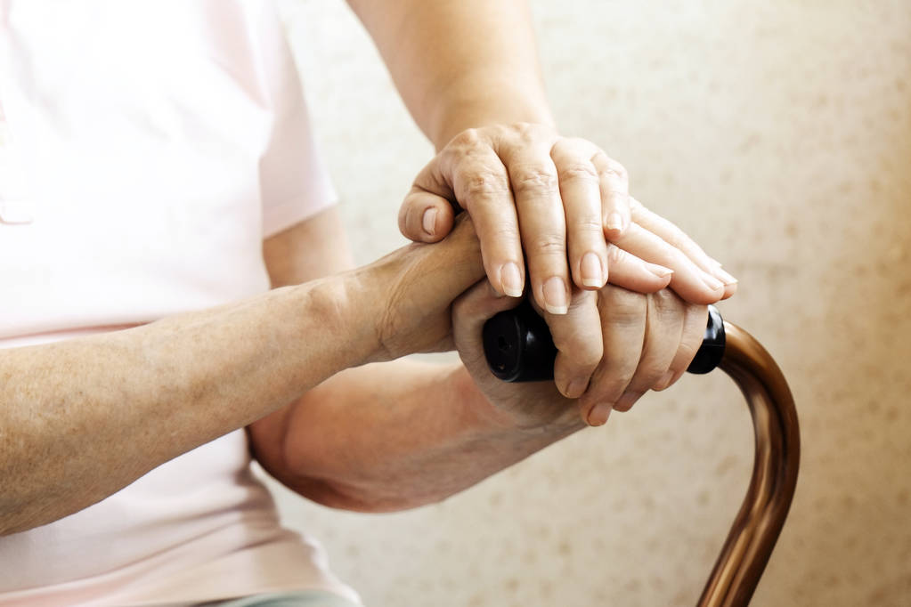 Senior kobietę 243rn uchwyt w podeszłym wieku opieki fecility. Szpital pielęgniarka pocieszające Starsza kobieta w domu opieki, siedząc z laską. Tło, na ręce z pomarszczona skóra z bliska. - Zdjęcie, obraz