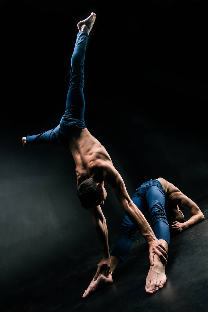 El dúo acrobático masculino realiza un complicado acto de equilibrio sobre un fondo oscuro
. - Foto, imagen
