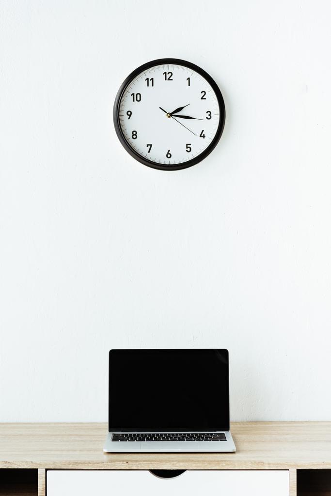 laptop on work desk under clock hanging on white wall - Photo, Image