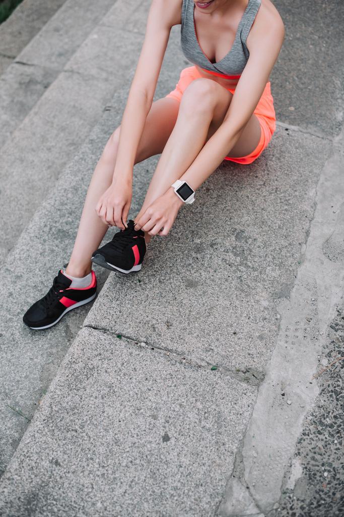 vista parcial de chica atlética atando cordones en zapatos deportivos mientras está sentado en las escaleras
 - Foto, imagen