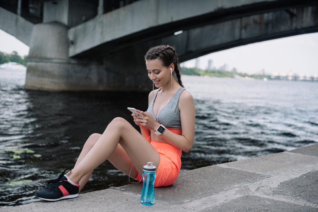 Junge Sportlerin nutzt Smartphone mit Kopfhörer und Smartwatch - Foto, Bild