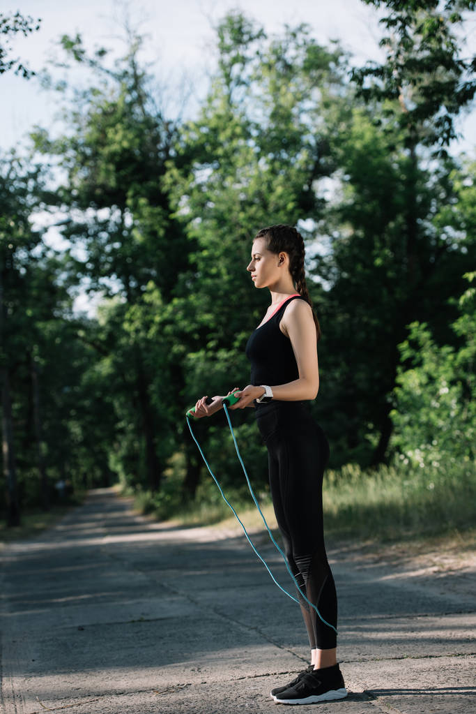 sportswoman exercising with jump rope on path in park - Photo, Image