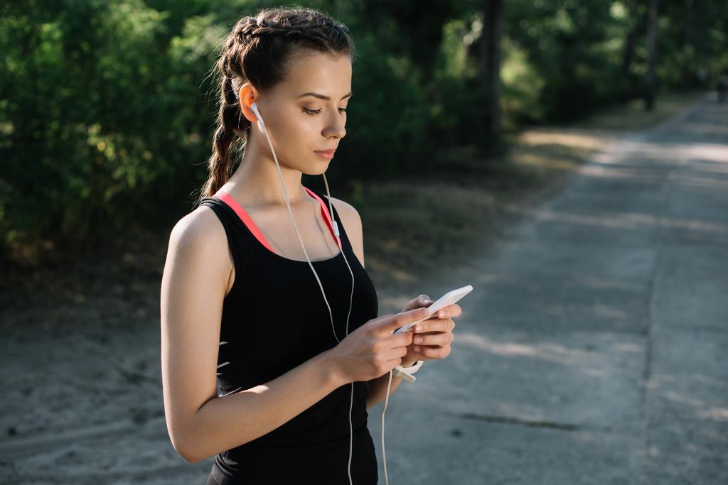 athletic woman listening music with earphones and using smartphone - Photo, Image