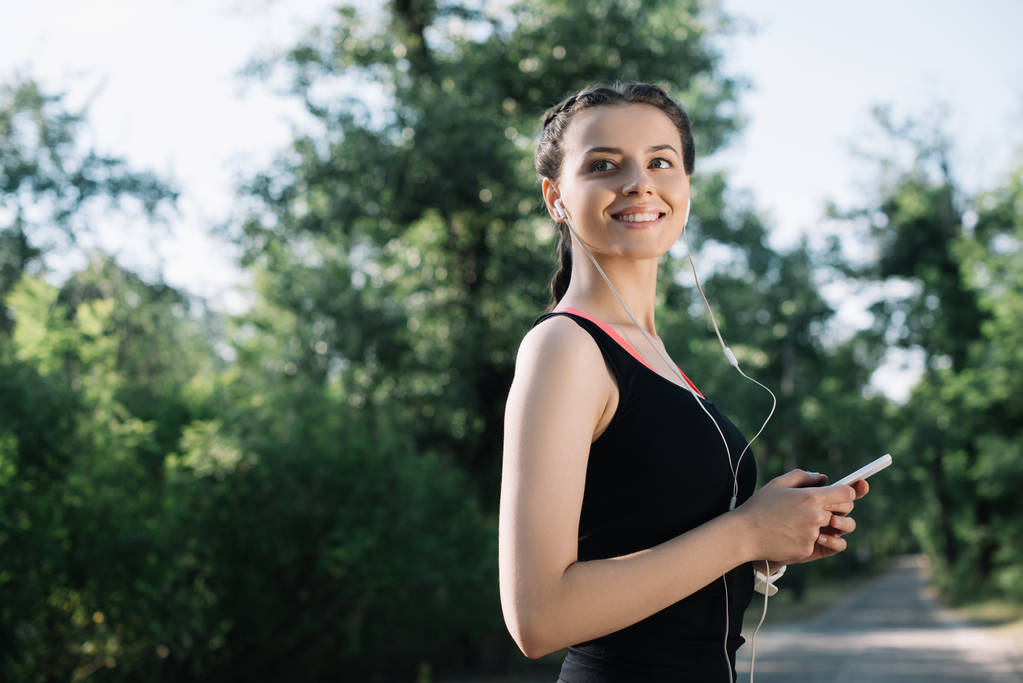 красива усміхнена спортсменка слухає музику з навушниками та смартфонами
 - Фото, зображення