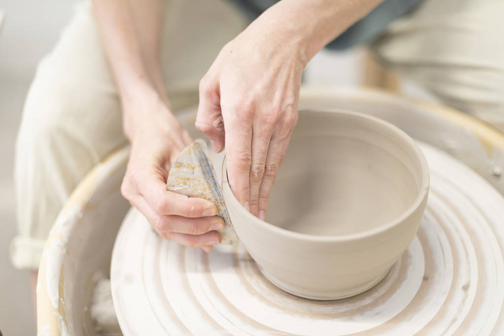 Jovem mulher sentada à mesa e fazendo argila ou caneca de cerâmica em seu estúdio de trabalho
 - Foto, Imagem