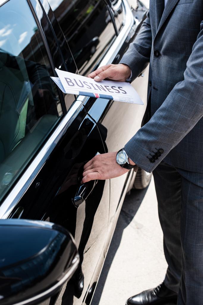 обрізаний знімок бізнесмена з газетою, що відкриває двері автомобіля на вулиці
 - Фото, зображення