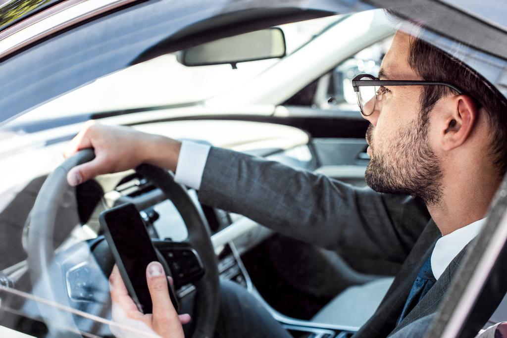 Zijaanzicht van zakenman met smartphone auto rijden - Foto, afbeelding