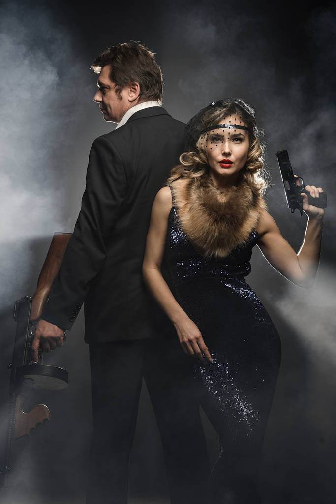 Un par de gángsteres, un hombre y una mujer con armas sobre fondo negro con humo
 - Foto, imagen