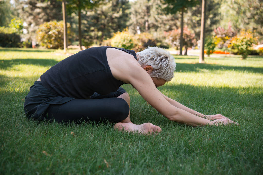 vista laterale della donna che pratica yoga in posa estesa bambino (Utthita Balasana) sull'erba nel parco
 - Foto, immagini