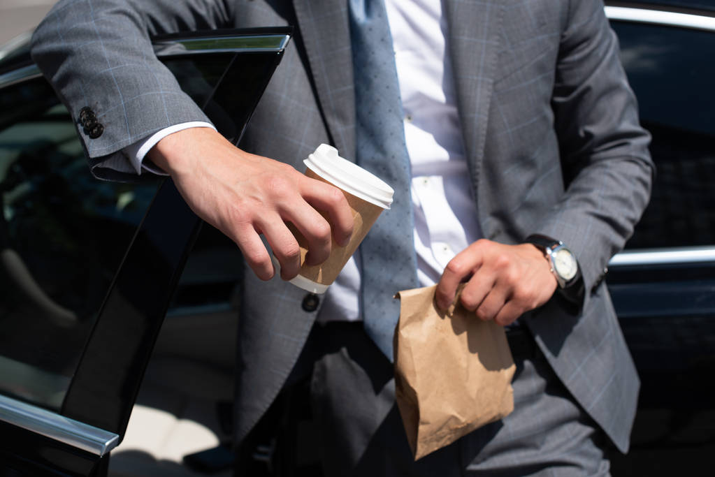 vista parziale di uomo d'affari con cibo da asporto e caffè per andare in piedi in auto
 - Foto, immagini