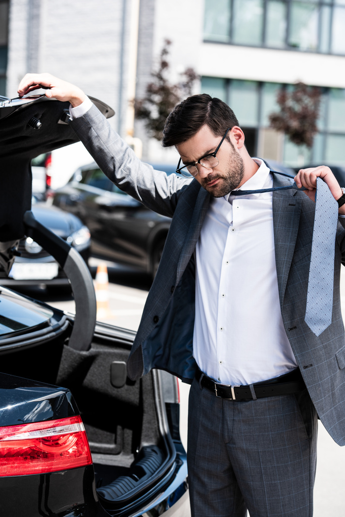 όμορφος επιχειρηματίας κλείσιμο πορτ-μπαγκάζ αυτοκινήτου και απογειώνεται γραβάτα στο δρόμο  - Φωτογραφία, εικόνα