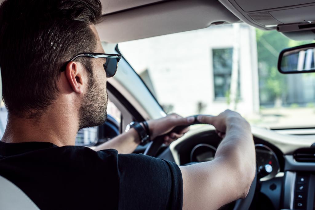 magabiztos fiatal stílusos férfi napszemüveg vezetői a kocsiját hátsó nézet  - Fotó, kép