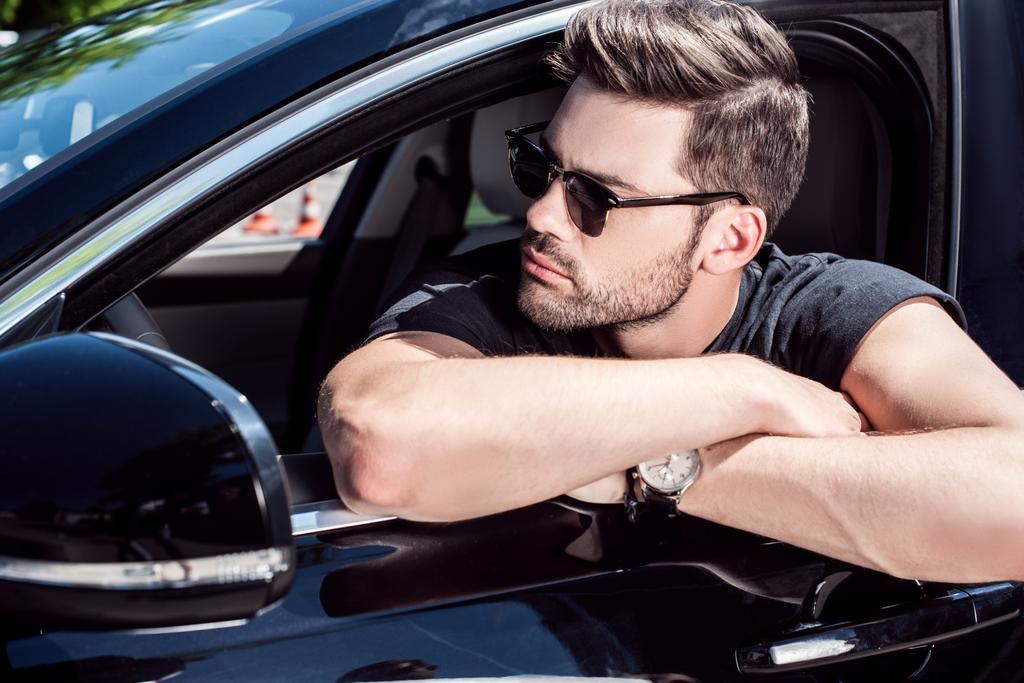 ritratto di un uomo serio ed elegante con gli occhiali da sole che distoglie lo sguardo mentre è seduto in macchina
  - Foto, immagini