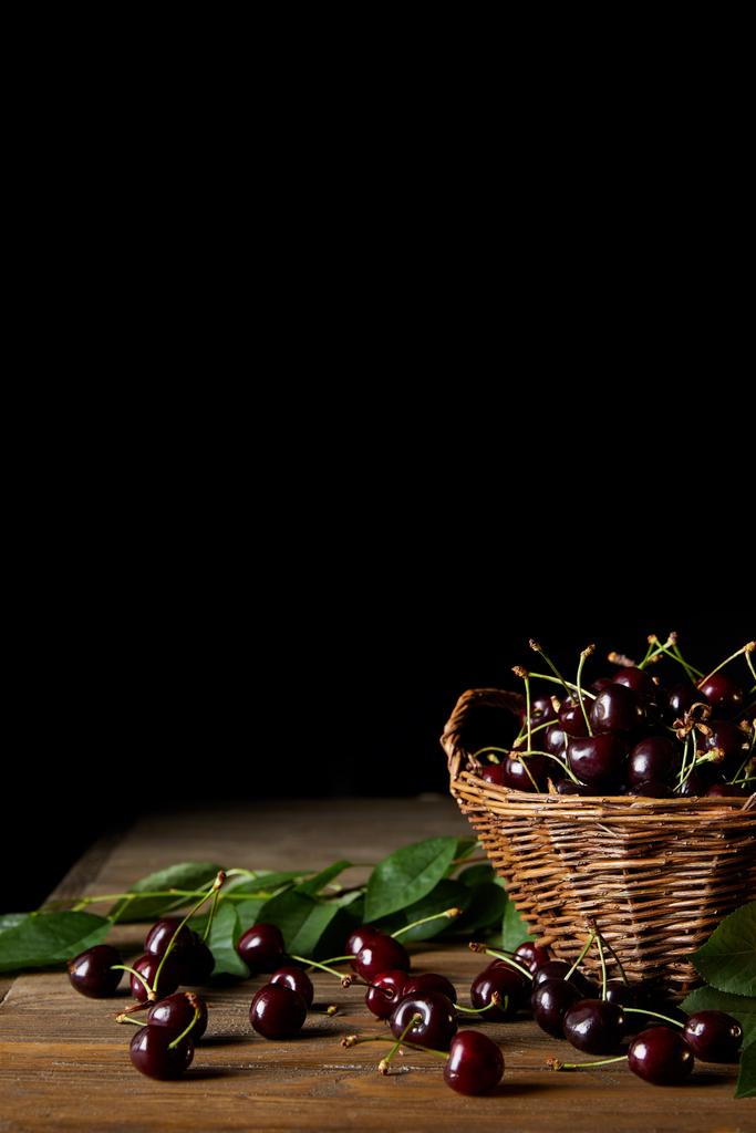 木製のテーブルと黒葉の古いバスケットで新鮮な収穫赤チェリー - 写真・画像