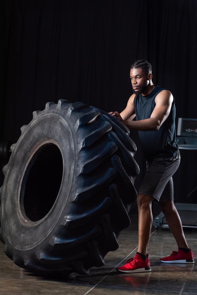 Ganzkörperansicht des athletischen afrikanisch-amerikanischen Mannes, der mit Reifen trainiert und wegschaut - Foto, Bild