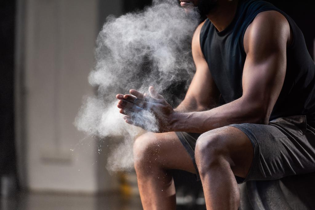 обрезанный кадр мускулистого африканского спортсмена, нанесшего тальк на руки
 - Фото, изображение