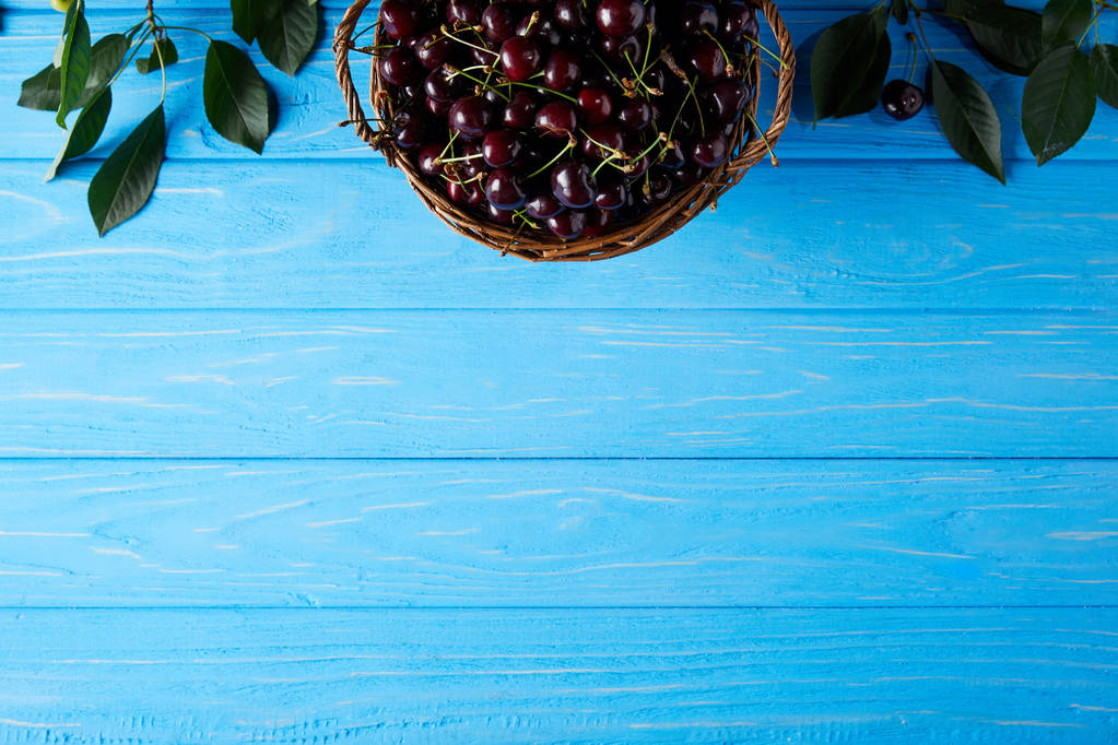 felülnézet, a kosár friss cseresznye a kék fa felülettel - Fotó, kép