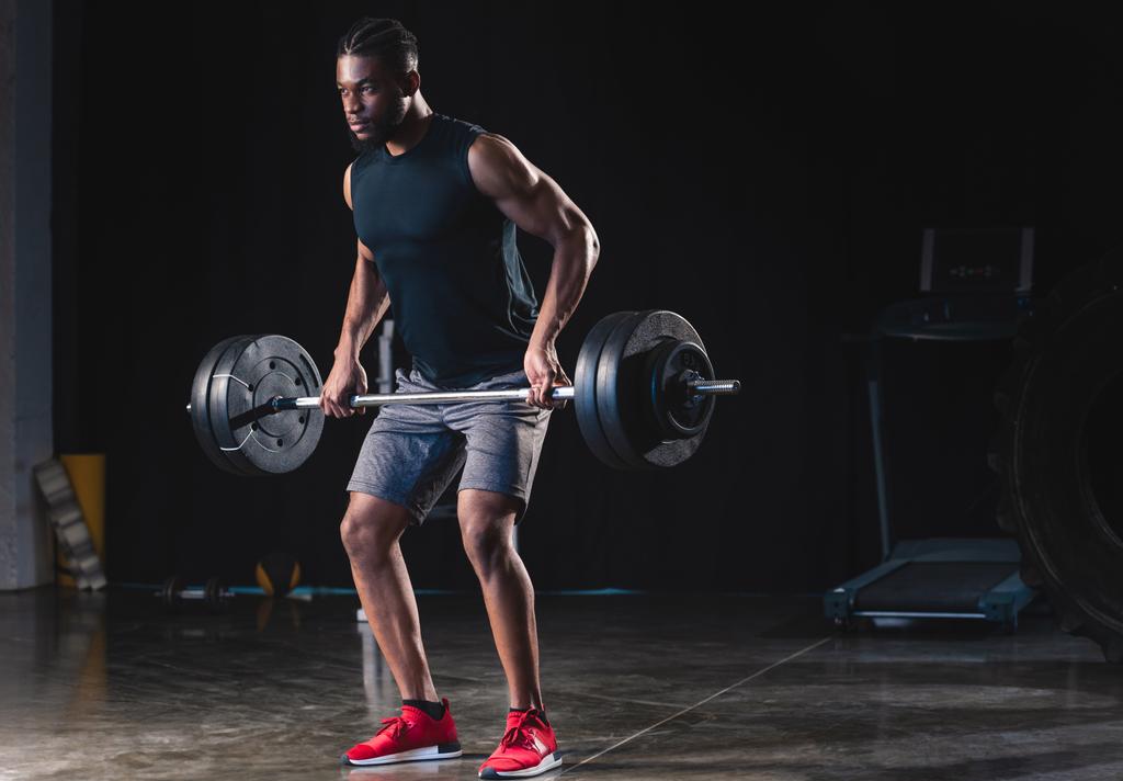 atletico uomo afroamericano in abbigliamento sportivo sollevamento bilanciere e guardando lontano in palestra
  - Foto, immagini