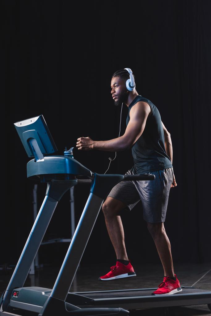 вид збоку красивий молодий афроамериканський спортсмен в навушниках, що працюють на біговій доріжці
 - Фото, зображення