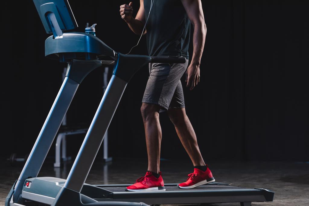 oříznuté záběr afroamerické muže v sluchátka trénink na běžeckém pásu - Fotografie, Obrázek