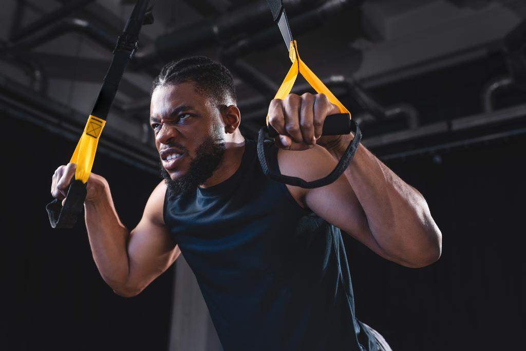 vista de ángulo bajo del entrenamiento de deportista afroamericano muscular con correas de fitness
  - Foto, Imagen