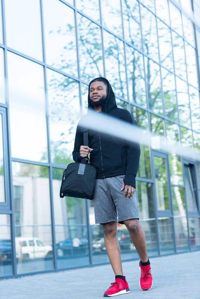 lage hoekmening van jonge african american man in sportkleding lopen met de tas op straat - Foto, afbeelding